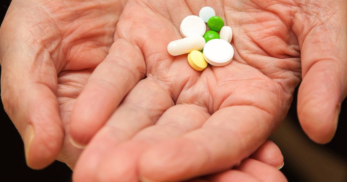 Two hands holding mix of white, green, and yellow pills