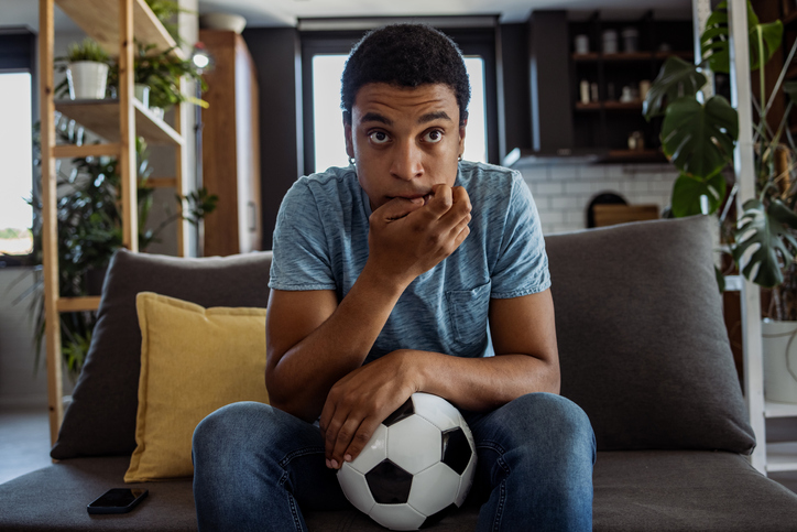 young man sitting on a sofa with a soccer ball chewing on finger nails